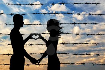 Refugees concept. Male and female refugees show hands symbol heart on the background of the fence barbed wire