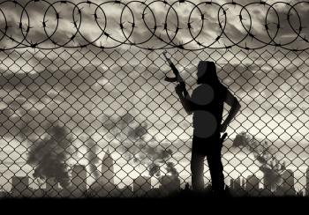 Terrorism and conflict. Armed terrorists near the fence of barbed wire and the city in smoke