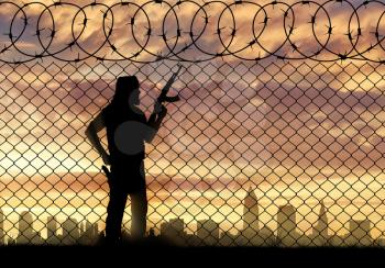 Terrorism and conflict. Armed terrorists near the fence of barbed wire and the city in the distance