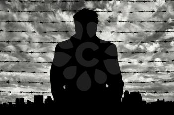 Refugees concept. Silhouette of refugee men near the border fence in the background of the urban landscape