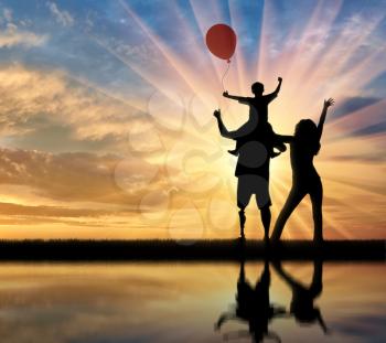 Happy disabled with prosthetic legs walking with his wife and child with balloon and reflection in water on sunset background. Concept happy disabled