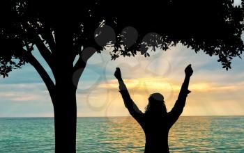Success and happiness concept .. Silhouette of a happy woman on a background of sea sunset under a tree