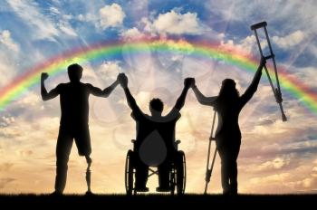 Invalids on crutches and in wheelchair and with prosthetic leg to stand on background of rainbow and sunset and holding hands. Concept happy disabled