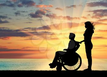  Concept of disability and disease. Silhouette of disabled person with a guardian on the sea sunset