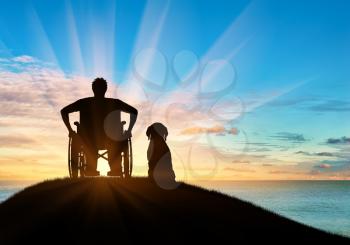 Concept of disability and disease. Silhouette of disabled person in a wheelchair with his dog at sunset and reflection in water