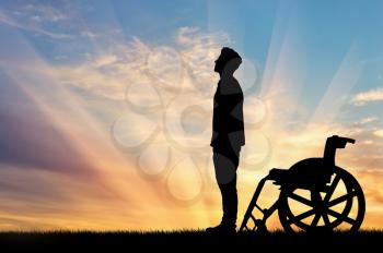 Concept of disability and disease. Silhouette of disabled person who stood out of the wheelchair on the sunset background