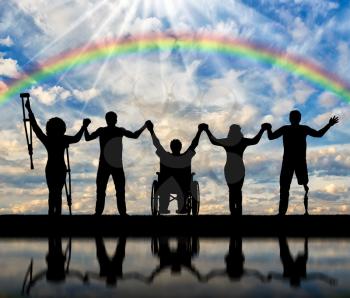 Invalids on crutches and in wheelchair and prosthesis in foot and healthy people standing on rainbow background and holding hands. Concept happy disabled
