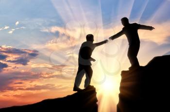 Man gives helping hand to friend over gorge sunset. Concept helping hand