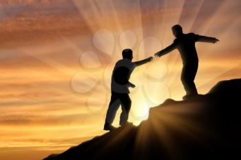 Man gives helping hand to friend when climbing on mountain. Concept helping hand