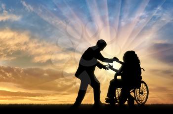 Man helps woman in wheelchair to stand up sunset. Concept help disabled persons