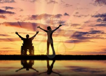 Concept of disability and disease. Silhouette happy disabled person in a wheelchair next to the guardian at sunset