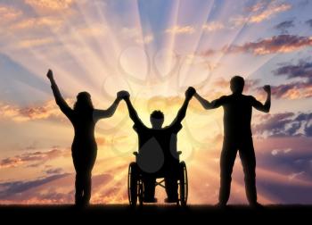 Disabled in wheelchair and healthy people holding hands on sunset background. Concept happy disabled