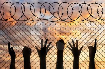 Refugees hands silhouette near the fence of barbed wire. refugee concept
