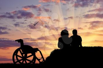 Concept of disability and disease. Silhouette of disabled person with the guardian at sunset background