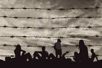 Concept of refugee. Silhouette of a crowd of refugees rest on the ground near the fence or barbed wire 