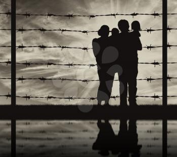 Concept of refugee. Silhouette of a family with children of refugees and fence with barbed wire and reflection