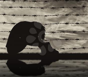 Concept of refugee. Silhouette Despair refugee woman near the fence of barbed wire and reflection