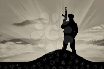 Concept of terrorism. Silhouette of a terrorist with a rifle standing on a pile of skulls at sunset