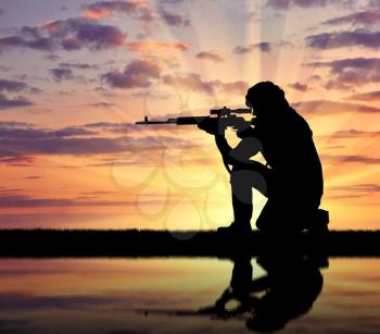 Silhouette of a terrorist with a weapon against a background of a sunset and reflection