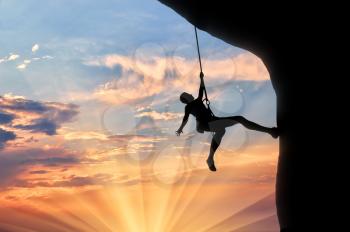 Climber on the rope climbs cliff sunset. Concept of mountaineering