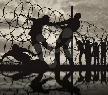  Concept of security. Silhouette of refugees climb over the barbed wire at the border and reflection