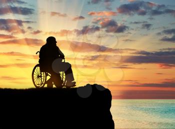 Concept of disability and old age. Silhouette of disabled person in a wheelchair on a hill against a sunset sea