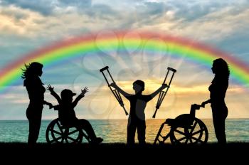 Happy boy in wheelchair and disabled boy standing with crutches near sea and nurses rainbow. Happy disabled child concept