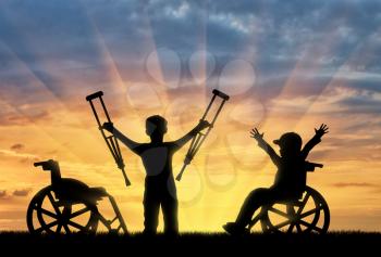 Happy boy in wheelchair and boy standing with crutches disabled person sunset. Happy disabled child concept