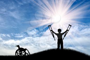 Disabled child standing with crutches alongside wheelchair on the hill day. Concept of disability