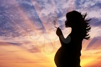 Concept of pregnancy and bad habits. Silhouette of a pregnant woman smokes a cigarette at sunset