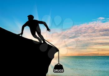 Concept of addiction. Silhouette of a man on a rock and drugs in the form of cargo on sea sunset background