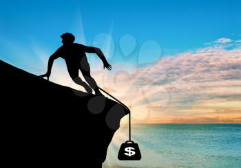 Concept of money. Silhouette of a man on a rock and the weight of the dollar against the backdrop of the sea sunset