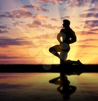 Concept of beauty and sports. Silhouette of bodybuilder posing at sunset and its reflection in water