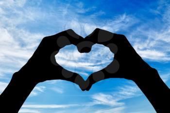 ?oncept of feelings and emotions. Silhouette of the heart hand gesture against a blue sky
