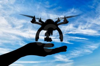 Silhouette of a drone and a human hand on a sky background