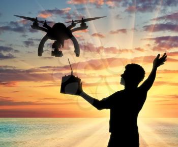 Silhouette of a flying drone, and a man with a remote control on a background of sea sunset. Concept quadrocopters