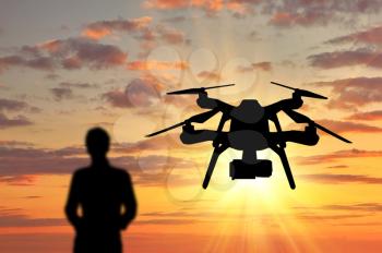 Silhouette of a flying drone, and a man with a remote control at sunset. Concept quadrocopters