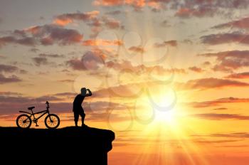  concept of recreation and tourism. Silhouette of a happy man on the mountain top with bike looking off into the distance at sunset
