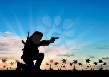 Concept of terrorism. Silhouette of a terrorist with a rifle on a background of sunset and palm trees