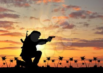 Concept of terrorism. Silhouette of a terrorist with a rifle on a background of sunset and palm trees