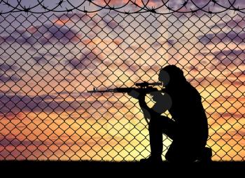 Concept of terrorism. Silhouette of a terrorist sniper near the border fence in the sunset