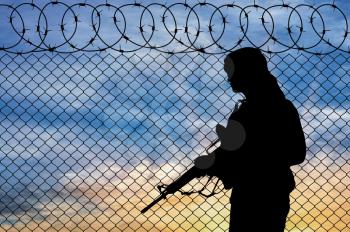 Concept of terrorism. Silhouette terrorist near the border fence at sunset