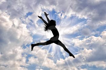 Concept of happiness and freedom. Silhouette of happy girl jumping on a background of a beautiful sunny sky