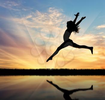 Concept of happiness and freedom. Silhouette of happy woman jumping at sunset and reflection in water