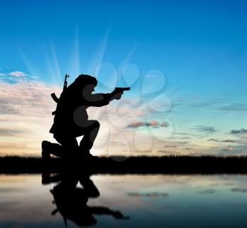 Silhouette of a terrorist with a rifle on a background of sky and reflection in water