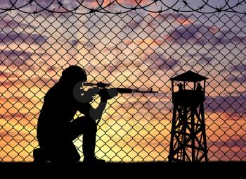 Concept of terrorism. Silhouette of a terrorist sniper near the border fence and watchtower at sunset