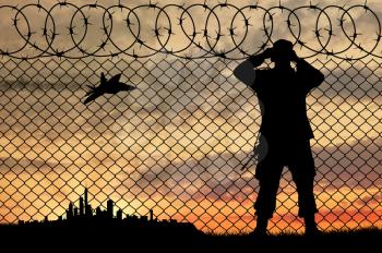 Concept of terrorism. Silhouette of a terrorist near the fence to follow the city at sunset