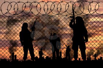 Concept of terrorism. Silhouette terrorists near the border fence in the background on the city in smoke at sunset