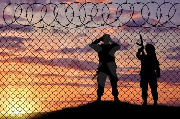 Concept of terrorism. Silhouette scouts terrorists near the border fence in the sunset