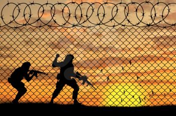 Concept of terrorism. Silhouette scouts terrorists near the border fence in the sunset